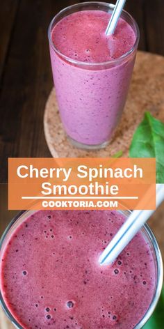 two glasses filled with berry spinach smoothie on top of a wooden table next to green leaves