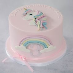 there is a pink cake with a unicorn on top and a rainbow in the middle