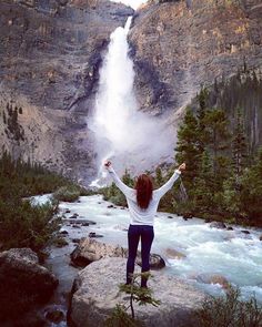 a woman standing at the base of a waterfall with her arms wide open in front of it