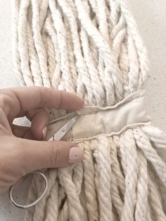 someone is cutting through the ends of a white rope with scissors and yarn ball in the background