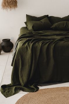 a bed with green sheets and pillows in a room next to two vases on the floor