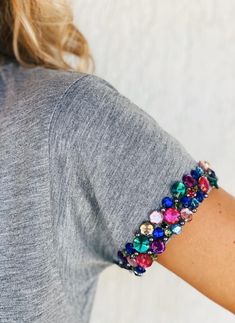 a woman wearing a gray shirt with colorful beads on it's arm and wrist