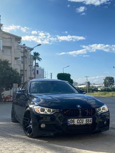 a black car is parked on the side of the road near some buildings and palm trees