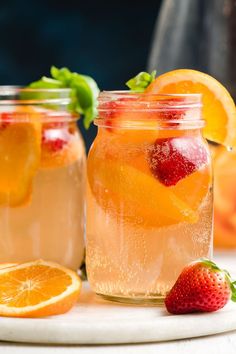 two mason jars filled with white wine sangria next to sliced oranges and strawberries