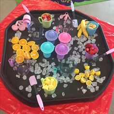 a tray filled with plastic cups and fruit sitting on top of a red table cloth