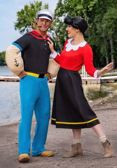 a man and woman dressed in costumes standing next to each other on the beach near water