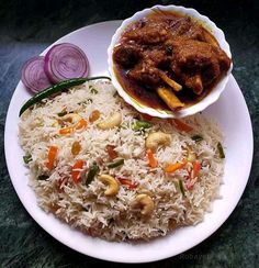 a white plate topped with rice and meat next to a bowl of red onion curry