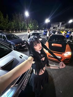 a woman with long black hair standing next to a car in a parking lot at night