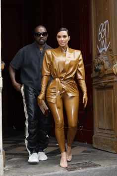 a man and woman are walking out of a building wearing brown leather outfits with white sneakers