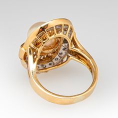 This radiant ring features an oval shaped gallery accented with one (1)  saltwater Akoya pearl, and a halo of twenty (20) bead set round brilliant cut diamond accents. The ring measures 21.6mm at the top, rises 10.7mm above the finger, tapering to 3.0mm wide and 1.0mm thick at the base of the shank.   It is crafted in 18k yellow gold and is currently a size 4.75.  The ring matches perfectly with the earrings under sku ab73326. Luxury Yellow Gold Pearl Ring With Round Cut, Akoya Pearl Ring, Radiant Ring, Saltwater Pearls, Swirl Ring, Pearl And Diamond Ring, Oval Face, Bead Set, Oval Faces