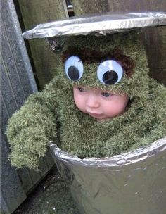 a small child wearing a green frog costume in a trash can with googly eyes