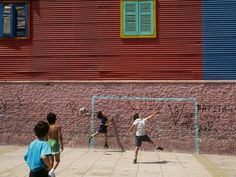 four people playing soccer in front of a red building with graffiti on the side wall