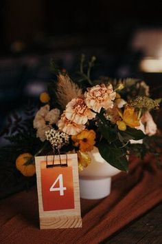 an arrangement of flowers on a table with a number 4 sign attached to the vase