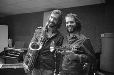 two men standing next to each other holding saxophones in front of a recording equipment