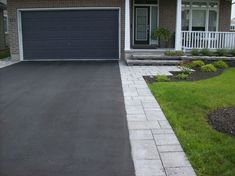 a driveway in front of a house with grass and flowers on the side walk next to it