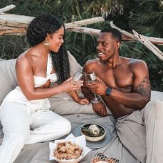 a man and woman sitting on a couch holding wine glasses in front of each other