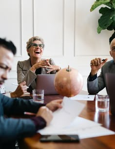 three people sitting at a table with laptops and papers in front of them, laughing