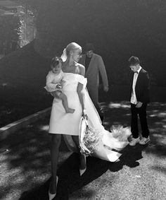 a woman in a white dress is walking with two men and a baby on her back