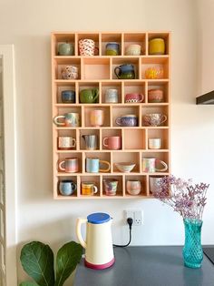 a wooden shelf filled with cups and vases on top of a counter next to a green plant