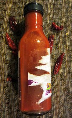 a bottle that is sitting on the ground with some chilis around it and other things surrounding it