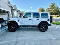 a white jeep is parked in front of a garage with the door open and it's tire rims missing