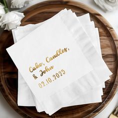 three napkins with gold foil on them sitting on a wooden plate next to white flowers