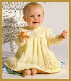 a baby wearing a yellow knitted dress and holding a piece of fruit in it's hand