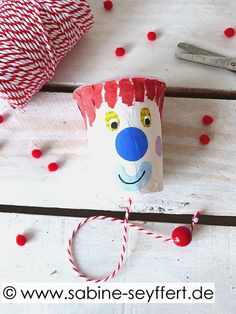 a paper cup with a clown face on it next to some spools of twine