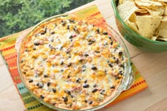 a casserole dish with black beans and corn in it next to a bowl of tortilla chips