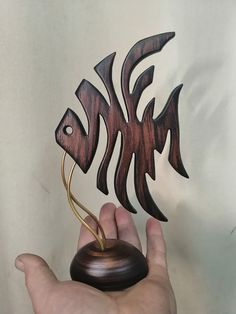 a hand holding a small wooden fish on top of a metal object in front of a white wall