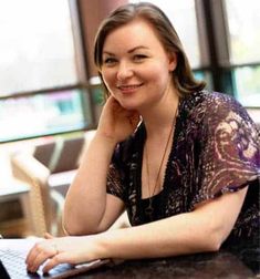 a woman sitting at a table with a laptop computer in front of her, smiling