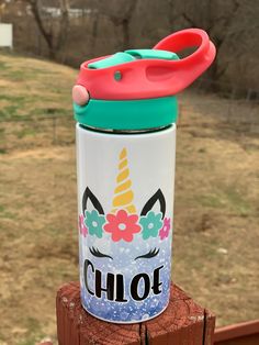 a cup with a lid and handle sitting on top of a wooden post next to a fence