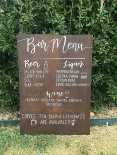 a wooden sign sitting in front of a lush green bush with writing on it's side