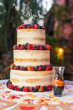 a three tiered cake with berries on top and the word love spelled in cursive writing