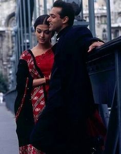 a man and woman standing next to each other on a bridge with buildings in the background