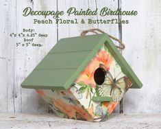 a green birdhouse sitting on top of a white wooden fence with flowers and butterflies painted on it