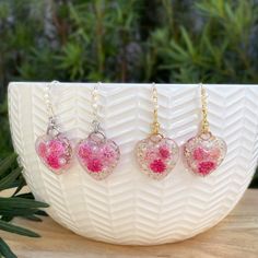 three pink heart shaped glass beads hanging from gold filled chain necklaces on a white plate