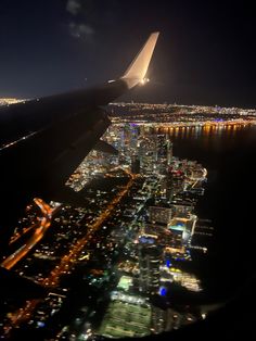 an airplane wing flying over a large city at night with lights on it's sides