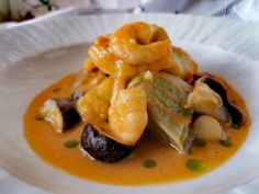 a white plate topped with shrimp and vegetables on top of a sauce covered tablecloth