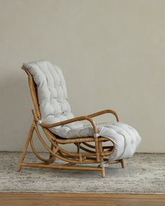 a chair with a cushion on it sitting in front of a white wall and rug