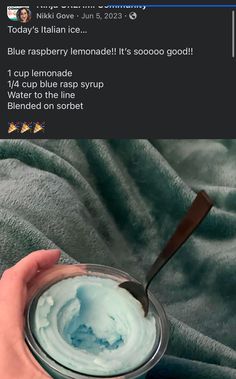 someone holding a spoon in their hand over a jar of blue lemonade whipped cream