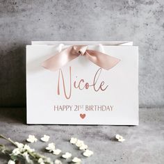 a white card with a pink bow on it that says nicole happy 21st birthday next to some flowers