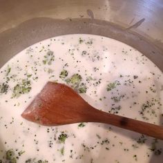 a wooden spoon in a pot full of broccoli and cheese sauce on the stove