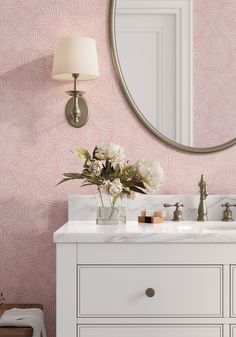 a bathroom vanity with pink wallpaper and white cabinetry, along with a round mirror over the sink