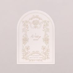 a white and gold wedding menu on a gray background with an arch in the middle