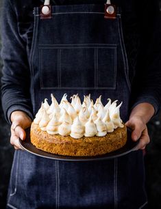 a person in an apron holding a cake with meringue on top and white icing