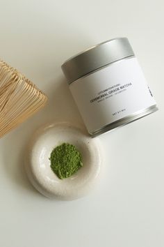 a white bowl with green powder next to a bamboo basket and a jar of matchsticks