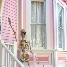 a skeleton is standing on the front steps of a pink house with a feathered tail