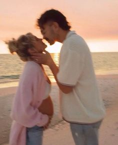 a man and woman kissing on the beach at sunset with water in the back ground