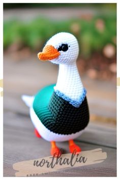 a crocheted duck sitting on top of a wooden table next to a name tag